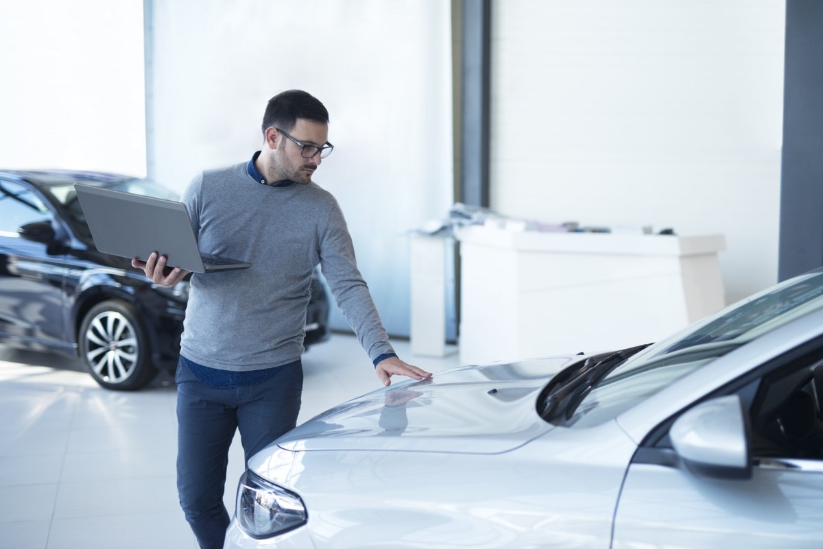 car-salesperson-with-laptop-checking-vehicle-specifications-local-dealership-showroom-min
